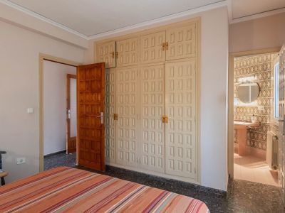 Schlafzimmer mit großem, hellem Einbauschrank mit Kassettentüren und dunklem Terrazzoboden, mit direktem Zugang zu einem gefliesten Badezimmer.