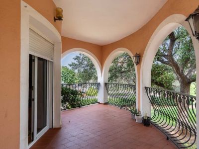 Überdachte Bogenterrasse mit Terrakotta-Bodenfliesen und schmiedeeisernem Geländer, das den Blick auf den grünen Garten freigibt.