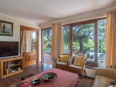 Wohnzimmer mit Fliesenboden und großen Holzfenstern mit Blick auf den Garten. Ausgestattet mit Ledersofa, Korbsesseln und direktem Zugang zum Außenbereich.