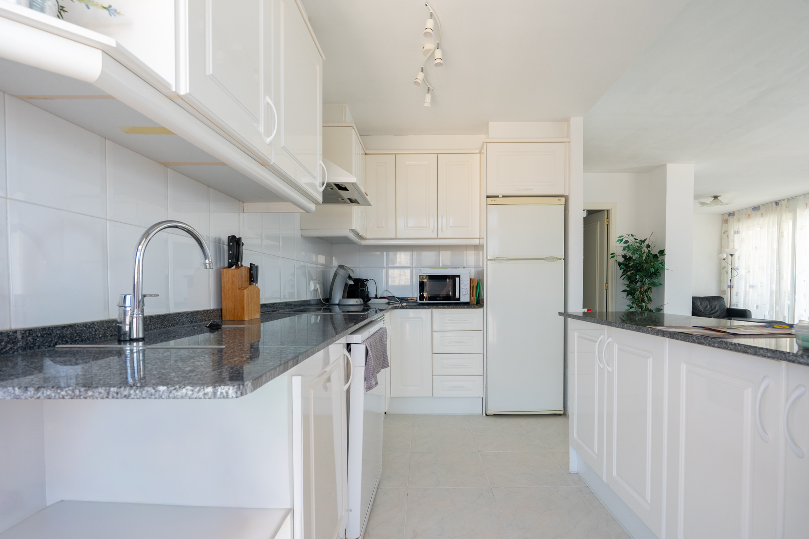 Funktionale Küche mit weißen Schränken, dunklen Granitarbeitsplatten und weißem Fliesenspiegel. Ausgestattet mit wichtigen Geräten und einer Halbinsel zum Wohnbereich.