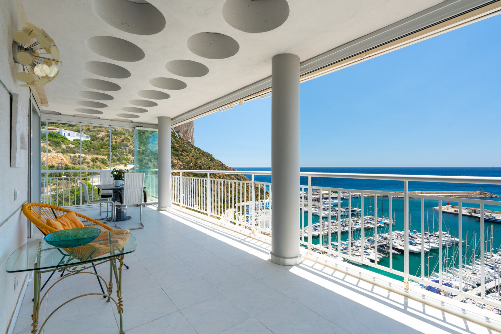 Geräumige, geflieste Terrasse mit einzigartigen runden Deckendetails, die einen Panoramablick auf den geschäftigen Hafen von Calpe und das Mittelmeer unter blauem Himmel bietet.