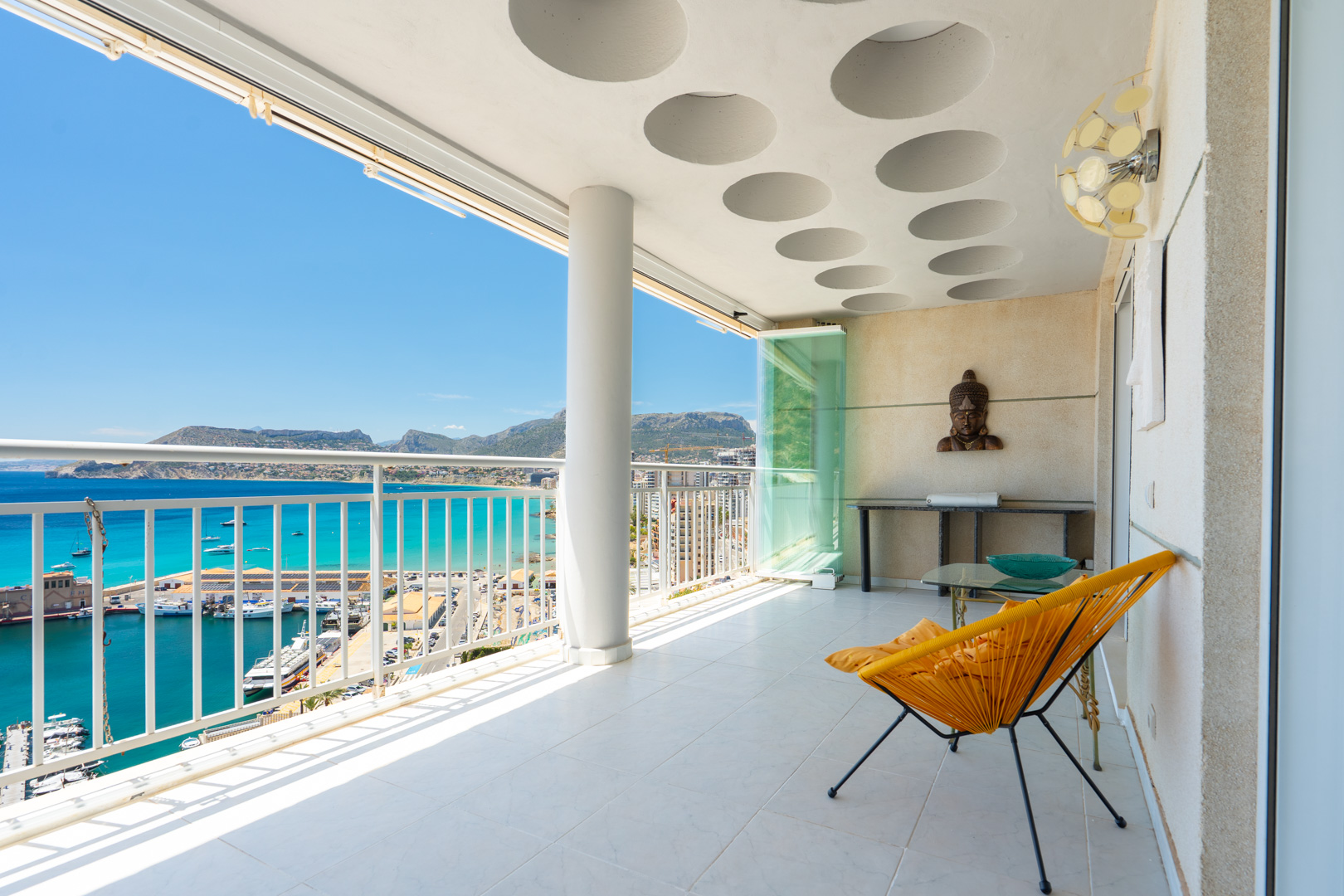 Großzügige überdachte Terrasse mit markanter runder Deckengestaltung und Glasvorhängen, mit Panoramablick auf Calpes Hafen, das türkisfarbene Meer und die Berge.