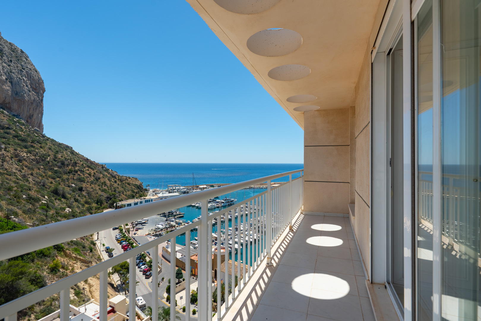 Helle Privatterrasse mit Fliesenboden, weißem Geländer und runden Deckenausschnitten. Bietet direkten Blick auf den Yachthafen, das Meer und den Peñón de Ifach.