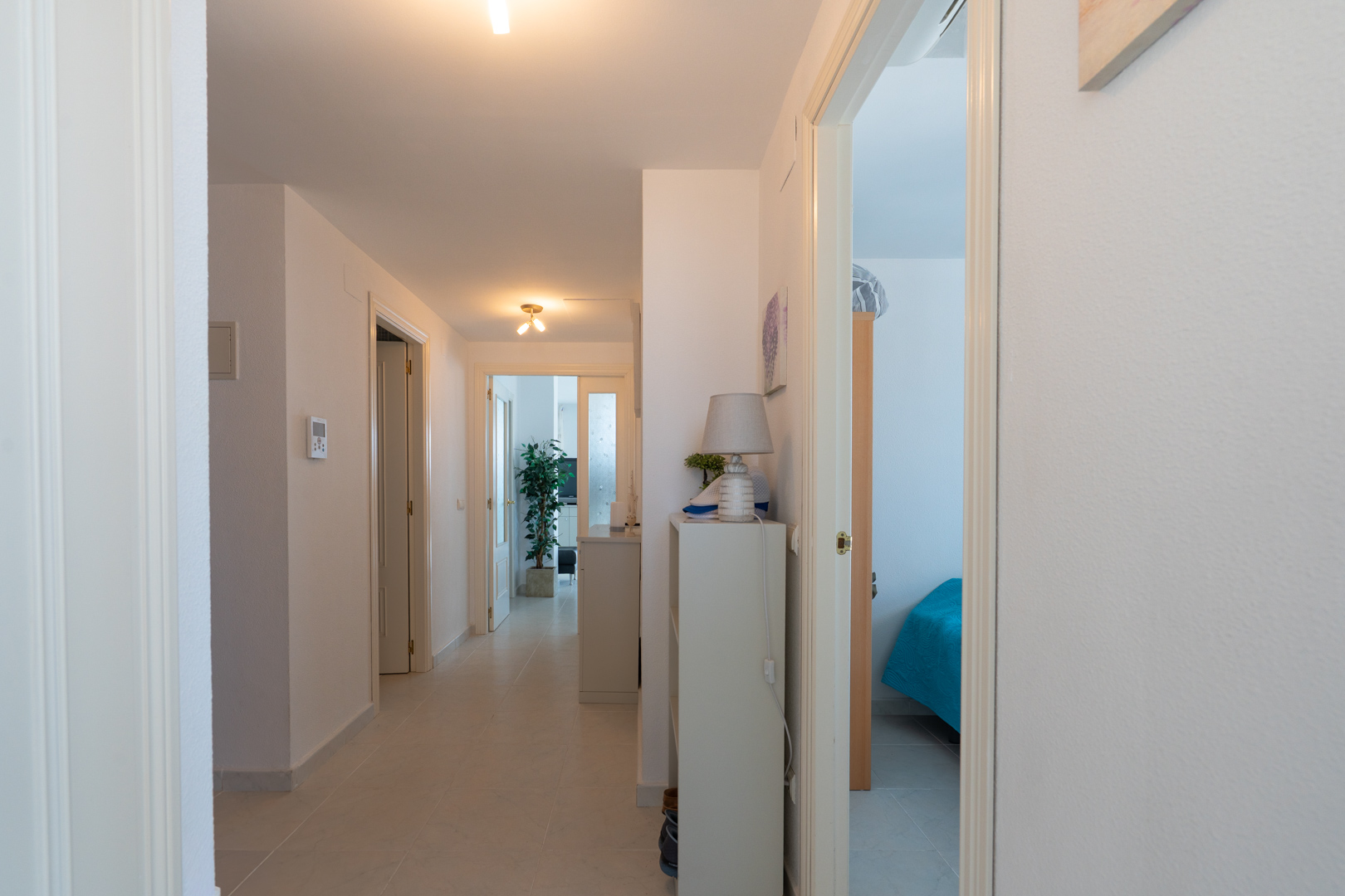 Heller Innenflur mit hellen Fliesen und weißen Wänden. Mehrere Türen führen zu Zimmern, darunter ein Schlafzimmer rechts und ein Wohnbereich im Hintergrund.