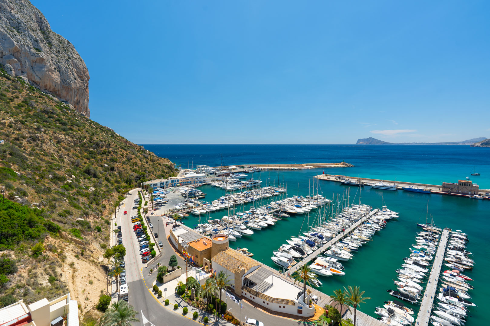Panoramablick auf den belebten Yachthafen von Calpe, eingerahmt vom majestätischen Peñón de Ifach und dem klaren türkisfarbenen Mittelmeerwasser.