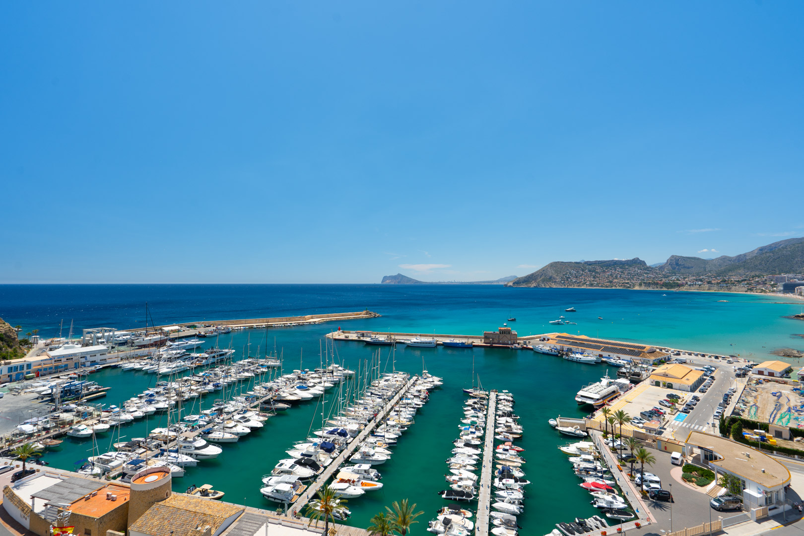 Panoramablick auf den Yachthafen von Calpe mit zahlreichen Booten im türkisfarbenen Wasser und der Mittelmeerküste bis zum Peñón de Ifach.