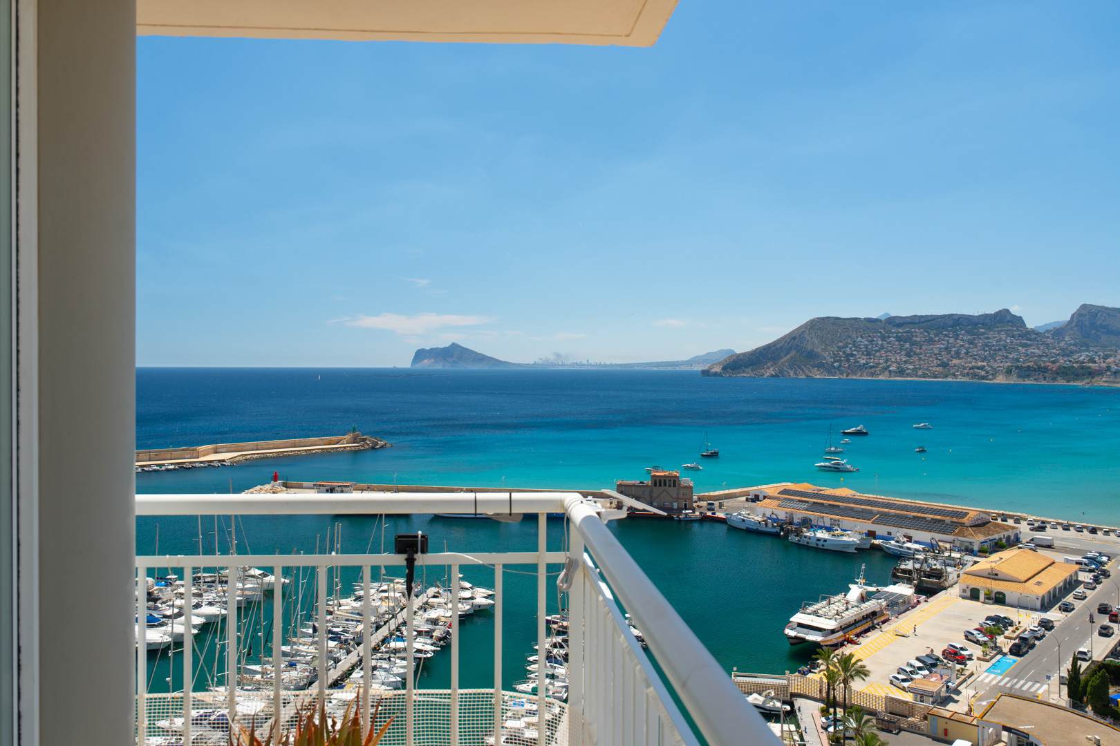Panoramablick vom Balkon auf den Yachthafen von Calpe, die türkisfarbene Bucht und ferne Küstengebirge unter klarem blauem Himmel.