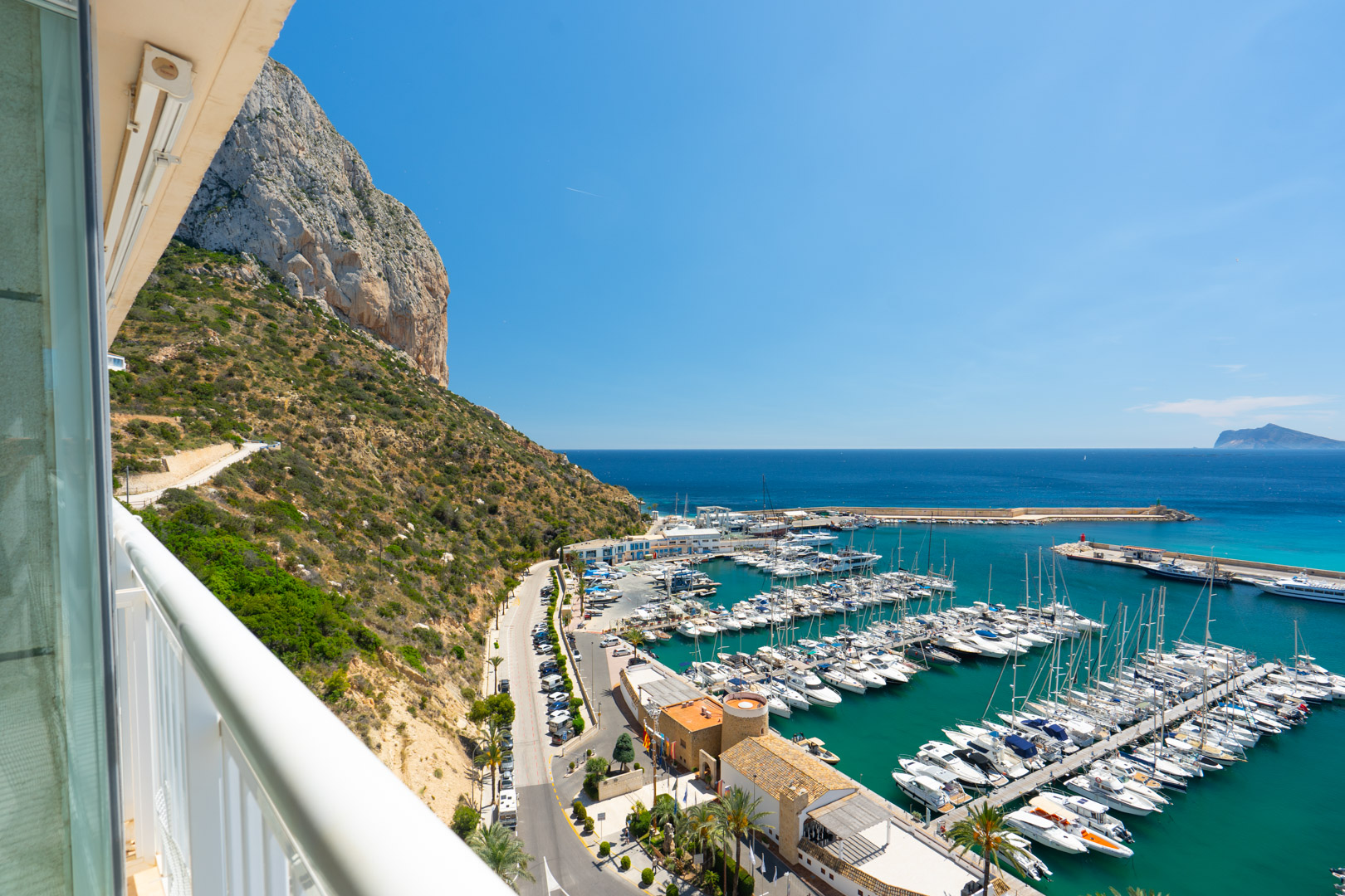 Panoramablick von der Terrasse auf den majestätischen Peñón de Ifach, den belebten Yachthafen von Calpe mit seinen Booten und das tiefblaue Mittelmeer.
