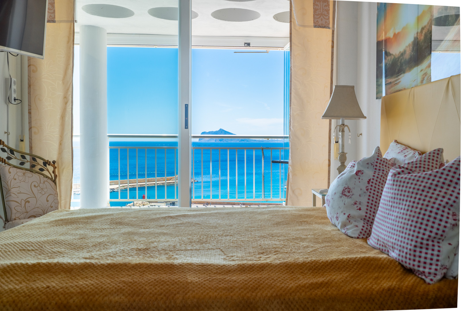Schlafzimmer mit gemütlichem Bett und direktem Zugang zu einer privaten Terrasse, mit Panoramablick auf das Meer, den Hafen und eine ferne Insel.