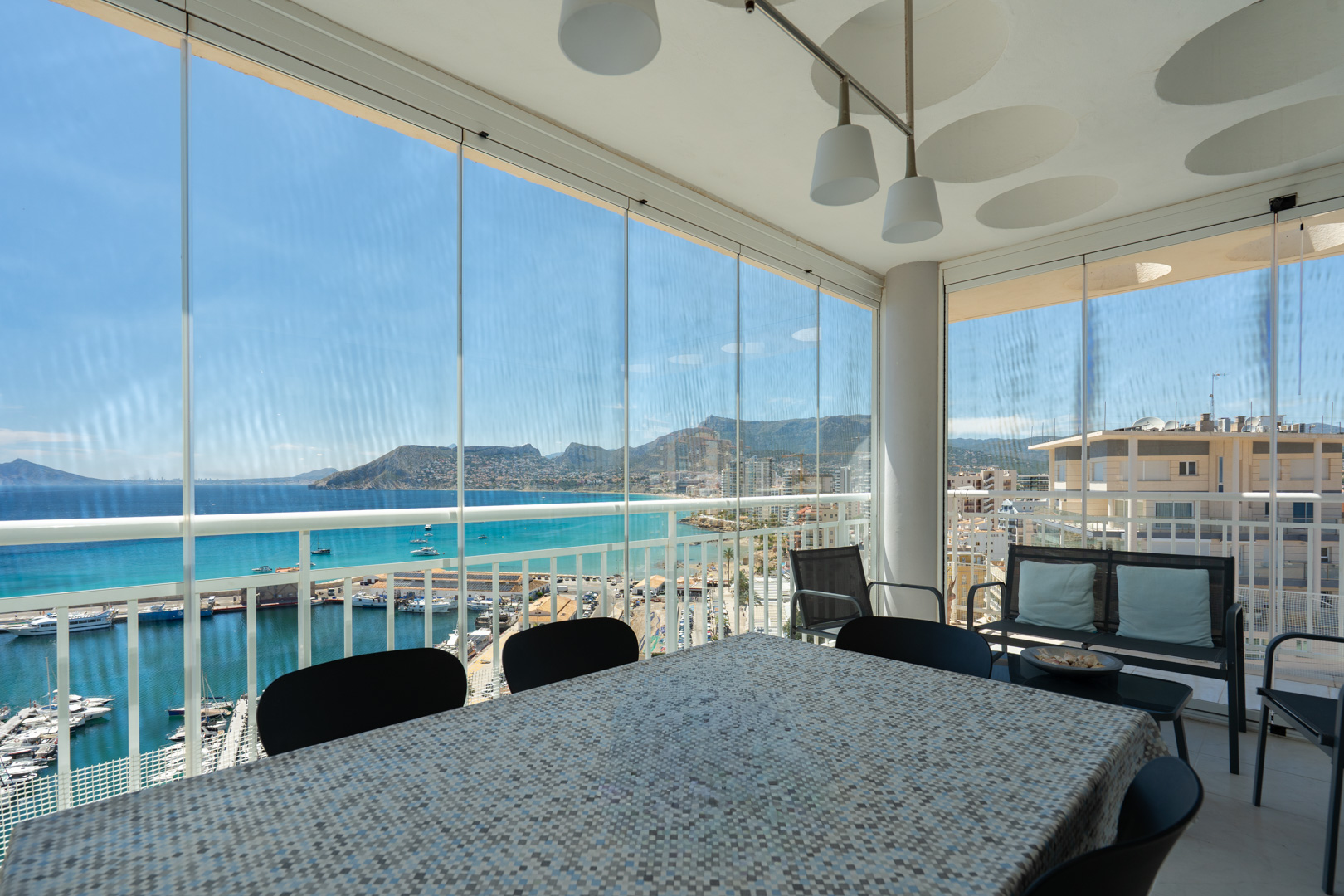 Verglaste Terrasse mit Essbereich, direkter Blick auf Calpes Yachthafen, das türkisfarbene Meer und den ikonischen Peñón de Ifach.