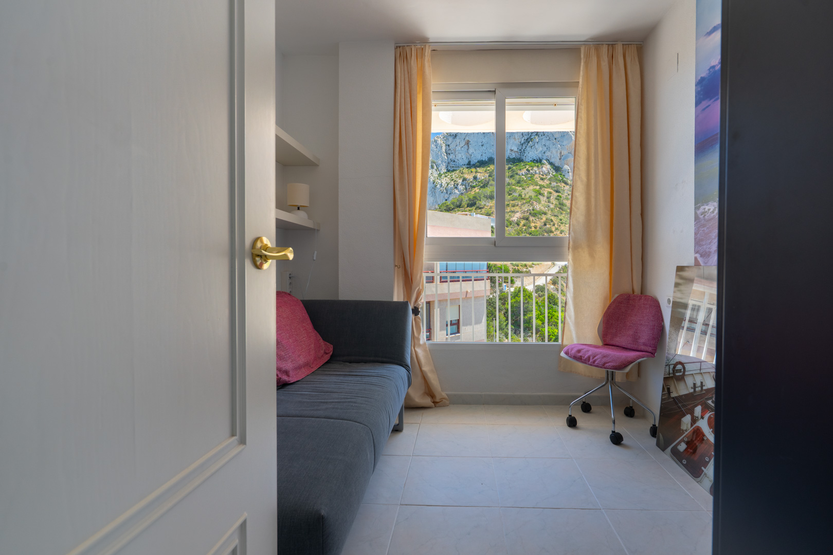 Zweites Schlafzimmer oder Arbeitszimmer mit Sofa, integrierten Regalen und Fensterblick auf den Peñón de Ifach Berg.