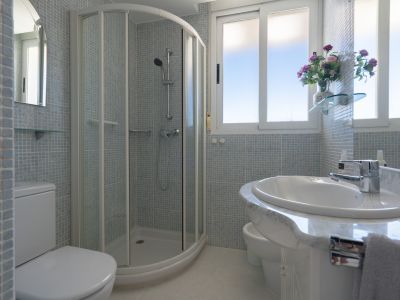 Badezimmer mit Eckdusche, WC, Bidet und Waschtisch mit Marmoroptik. Hellblaue Mosaikfliesen an den Wänden und Fenster für natürliches Licht.