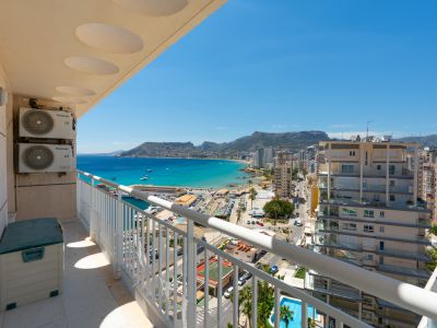 Balkon mit Panoramablick auf Calpes Yachthafen, die türkisfarbene Bucht und die Stadtküste, eingerahmt von einem weißen Geländer und externen Klimaanlagen.