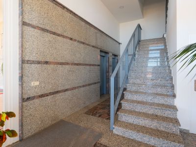 Der Gemeinschaftsbereich des Gebäudes zeigt polierte Granitwände mit dunklen Akzentstreifen, eine passende Granittreppe mit grauem Geländer und zwei Aufzüge, beleuchtet durch Einbaustrahler.