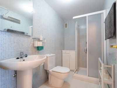 Funktionales Badezimmer mit hellblauen Mosaikfliesen, Standwaschbecken, WC, Duschkabine mit Milchglas und einem weißen Beistellschrank für Stauraum.