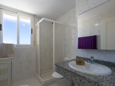 Funktionales Badezimmer mit weißen Marmor-Optik Fliesen, einem Waschtisch aus gesprenkeltem Granit mit ovalem Waschbecken, einer Eckdusche und Tageslichtfenster.