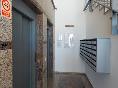 Gebäudeeingangshalle mit zwei Aufzügen, gerahmt von gesprenkeltem Granit, einem kontrastierenden dunklen Granitbodenstreifen, Gemeinschaftsbriefkästen und einer Metalltreppe.