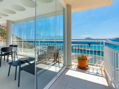 Geräumige Terrasse mit Glasschiebevorhängen, die einen Essbereich umschließen und direkten Blick auf den Yachthafen und die Bucht von Calpe bieten. Ein offener Bereich mit weißem Geländer und Pflanze ist sichtbar.