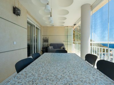Geräumige überdachte Terrasse mit Mosaik-Esstisch, Sitzgelegenheiten und Glasvorhängen, die Panoramablicke auf den Hafen, das Meer und die Berge freigeben.