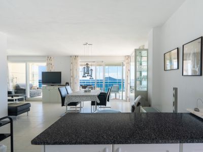 Geräumiger offener Wohn- und Essbereich mit moderner Pendelleuchte über dem Esstisch, hellen Fliesenböden und direktem Zugang zu einer Terrasse mit weitem Meerblick durch Glasschiebetüren.