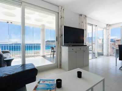 Geräumiger Wohnbereich mit Fliesenboden, TV-Möbel und Sofa, der sich zu einer verglasten Terrasse mit Panoramameerblick und gemusterter Decke öffnet.