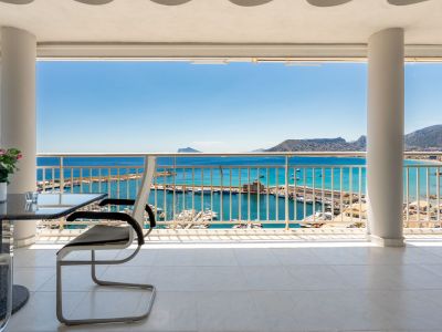 Großzügige überdachte Terrasse mit weißen Fliesen, die einen direkten Blick auf den Hafen von Calpe und das Mittelmeer bei strahlend blauem Himmel bietet.
