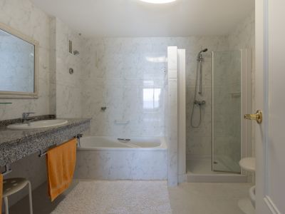 Hauptbadezimmer mit Doppelwaschtisch auf grauer Granitplatte, integrierter Badewanne und separater Duschkabine, komplett gefliest mit weißen Marmoreffekt-Fliesen.