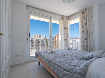 Helles Schlafzimmer mit Doppelbett, Einbauschrank und Glasschiebetüren zur Terrasse. Bietet klaren Stadtblick und blauen Himmel.