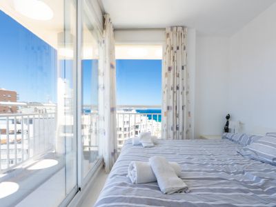 Helles Schlafzimmer mit Doppelbett und gestreifter Bettwäsche, direktem Zugang zur Terrasse und Panoramablick auf Meer und Himmel.