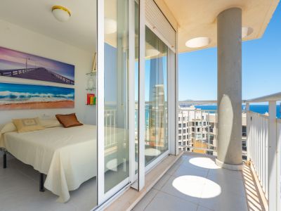 Helles Schlafzimmer mit Einzelbett und maritimer Wandkunst. Direkter Zugang zu einem privaten Balkon mit weißem Geländer, Betonsäule und Blick auf Meer und Küste.
