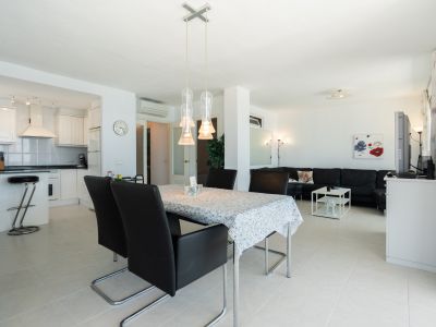 Offener Wohnbereich mit weißer Küche, Frühstücksbar, Essbereich mit moderner Pendelleuchte und Wohnzimmer mit schwarzem Ecksofa.