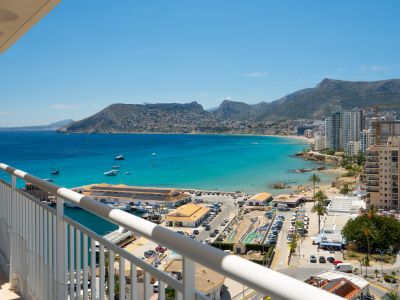 Panoramablick von der Terrasse auf den Hafen von Calpe, die türkisfarbene Bucht und die Küste mit Bergen im Hintergrund.