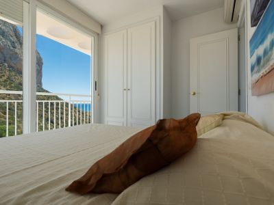 Schlafzimmer mit direktem Balkonzugang, mit Blick auf den markanten Peñón de Ifach, die grüne Hügellandschaft und das Mittelmeer. Ein weißer Einbauschrank ist vorhanden.