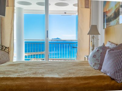 Schlafzimmer mit gemütlichem Bett und direktem Zugang zu einer privaten Terrasse, mit Panoramablick auf das Meer, den Hafen und eine ferne Insel.