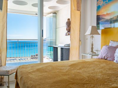 Schlafzimmer mit senfgelbem Bett und direktem Zugang zur verglasten Terrasse, die einen weiten Blick auf das Meer und den Hafen bietet.