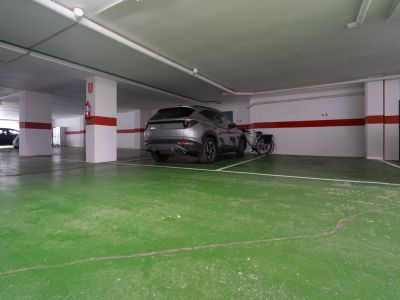 Zugewiesener Stellplatz in der Tiefgarage, mit grünem Betonboden und weißen Säulen mit roten Sicherheitsstreifen. Bietet Platz für ein Fahrzeug und ein Fahrrad.