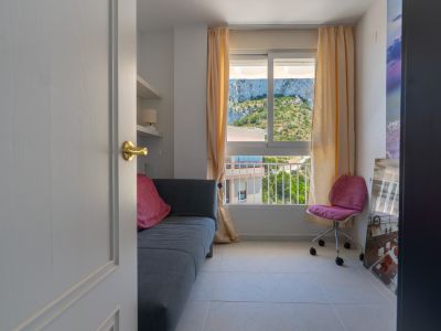 Zweites Schlafzimmer oder Arbeitszimmer mit Sofa, integrierten Regalen und Fensterblick auf den Peñón de Ifach Berg.