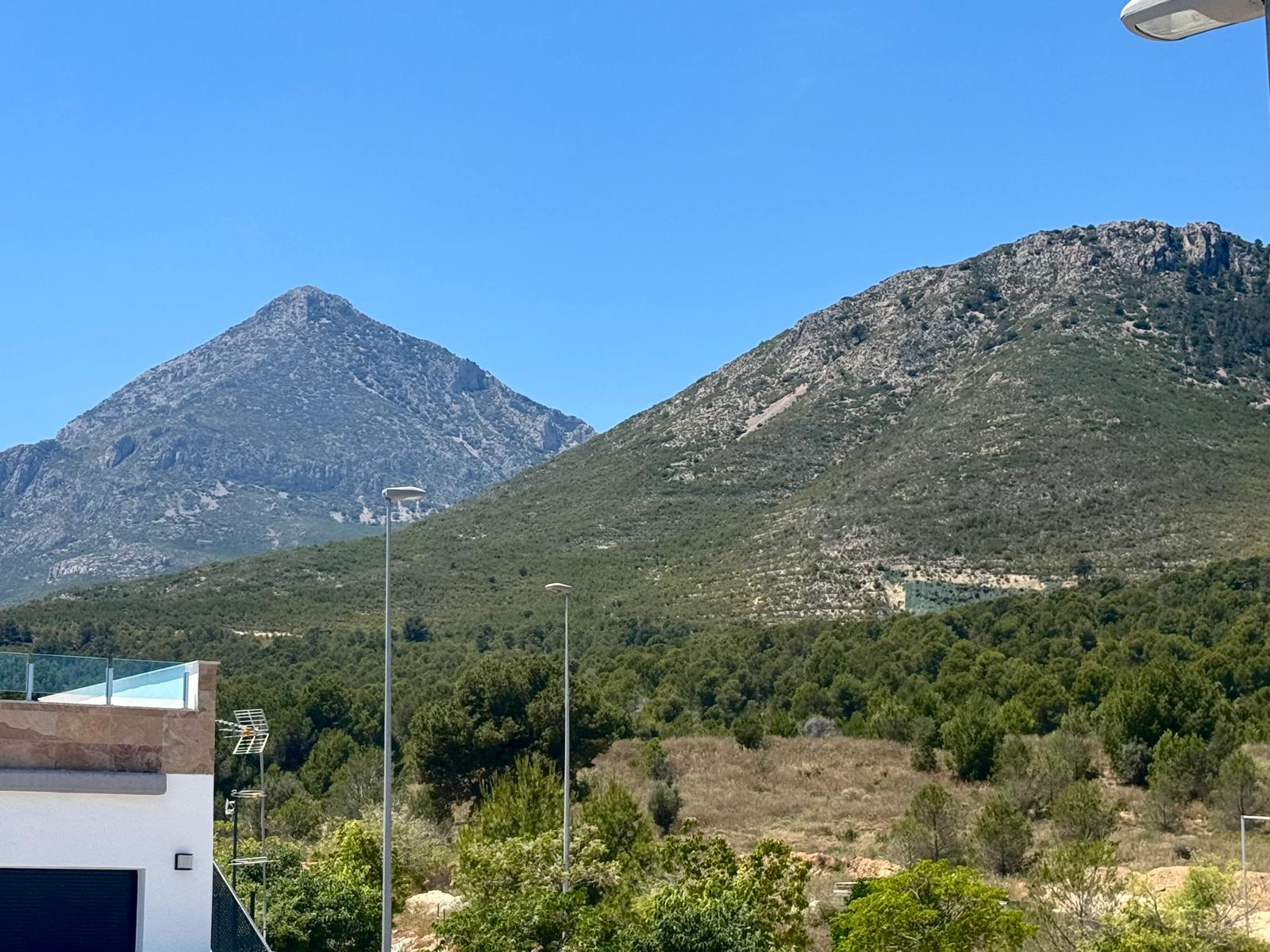 Freie Sicht auf zwei markante Felsberge und üppige mediterrane Vegetation, ergänzt durch eine moderne Terrasse mit Glasgeländer im Vordergrund.