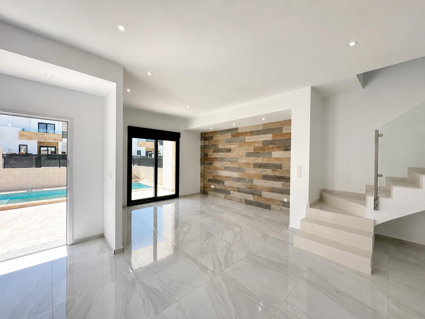 Geräumiger Wohnbereich mit polierten Porzellanfliesen, dekorativer Wandverkleidung in Holzoptik und direktem Zugang zum privaten Pool. Moderne Treppe mit Glasgeländer.