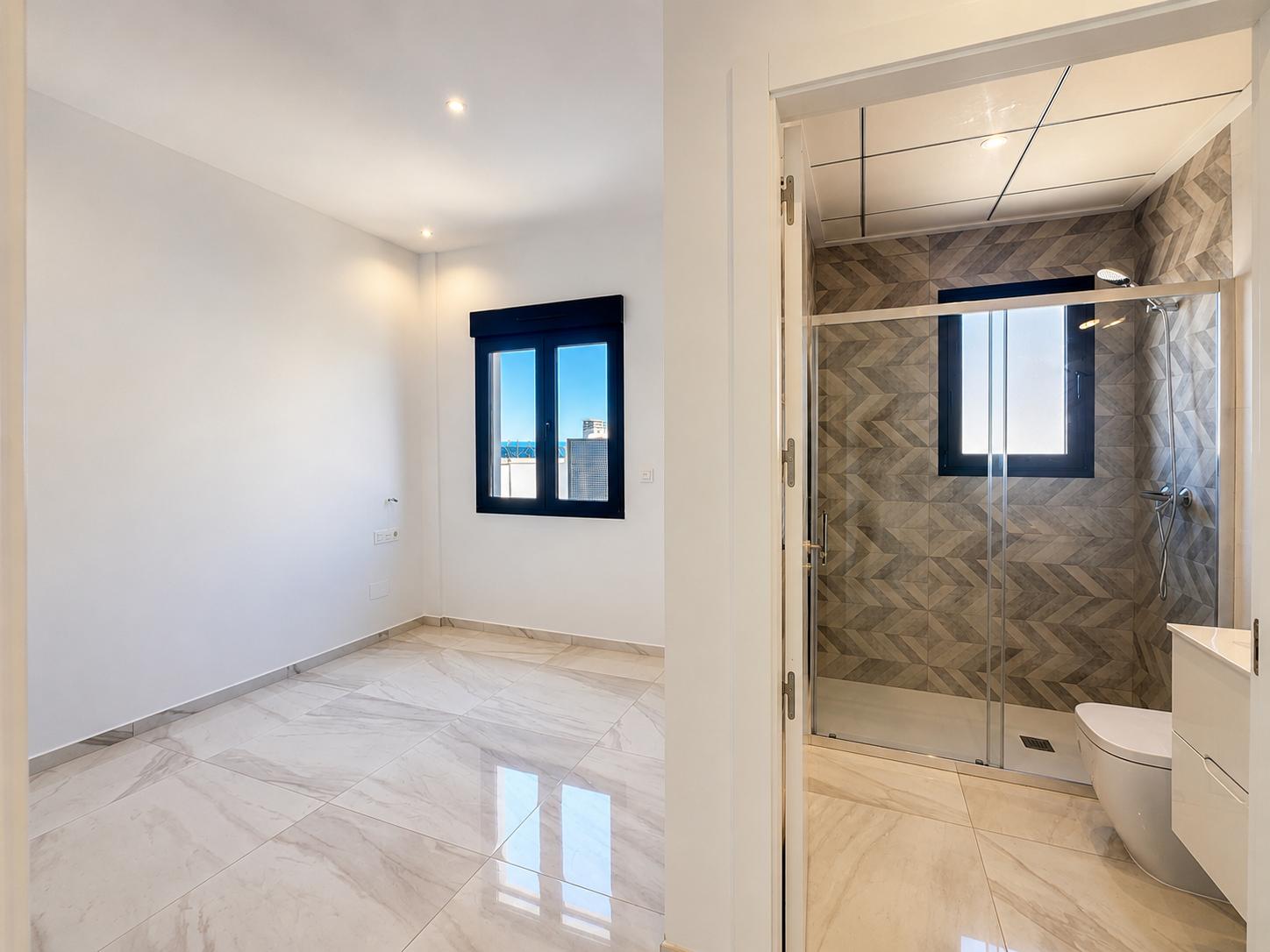 Geräumiges Schlafzimmer mit hellem Marmor-Effektboden und dunklem Fensterrahmen mit Fernblick, angrenzend an ein En-Suite-Bad mit geometrischen Duschwandfliesen.
