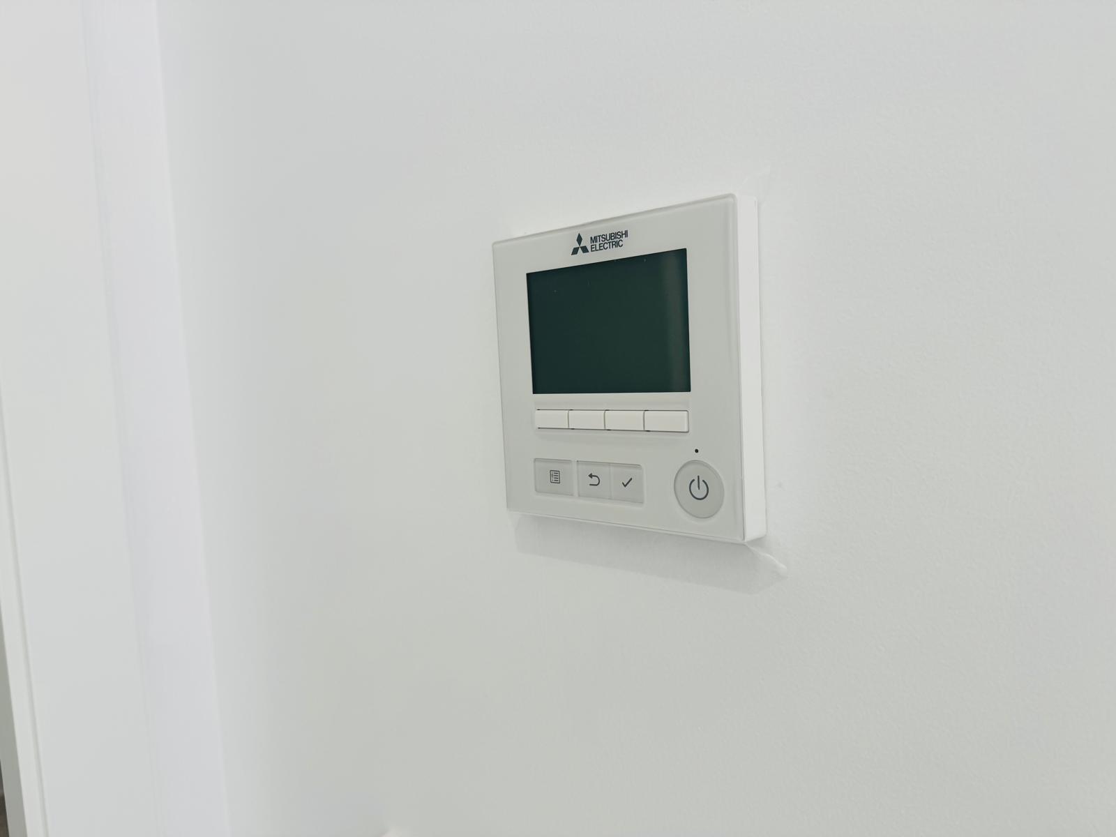 Mitsubishi Electric Bedienfeld für Kanalklimaanlage, mit Digitalanzeige und intuitiven Tasten, nahtlos in die weiße Wand integriert.