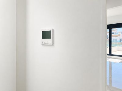 Ein elegantes digitales Klimabedienfeld ist an einer makellosen weißen Wand montiert, mit einem Blick in einen hellen Nebenraum und auf eine Außenterrasse.