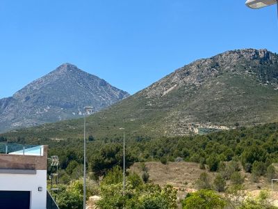 Freie Sicht auf zwei markante Felsberge und üppige mediterrane Vegetation, ergänzt durch eine moderne Terrasse mit Glasgeländer im Vordergrund.