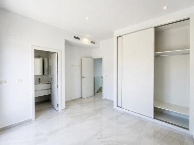 Geräumiges Schlafzimmer mit hellem Fliesenboden in Marmoroptik, Einbauschrank mit Schiebetüren und direktem Zugang zu einem modernen Bad en Suite. Deckenspots und Klimaanlagenkanäle.