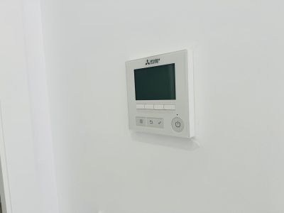 Mitsubishi Electric Bedienfeld für Kanalklimaanlage, mit Digitalanzeige und intuitiven Tasten, nahtlos in die weiße Wand integriert.