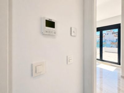 Mitsubishi Klimaanlagen-Bedienfeld und moderne Lichtschalter an einer weißen Wand, neben großen Schiebetüren, die zu einer gefliesten Terrasse mit Glasgeländer führen.