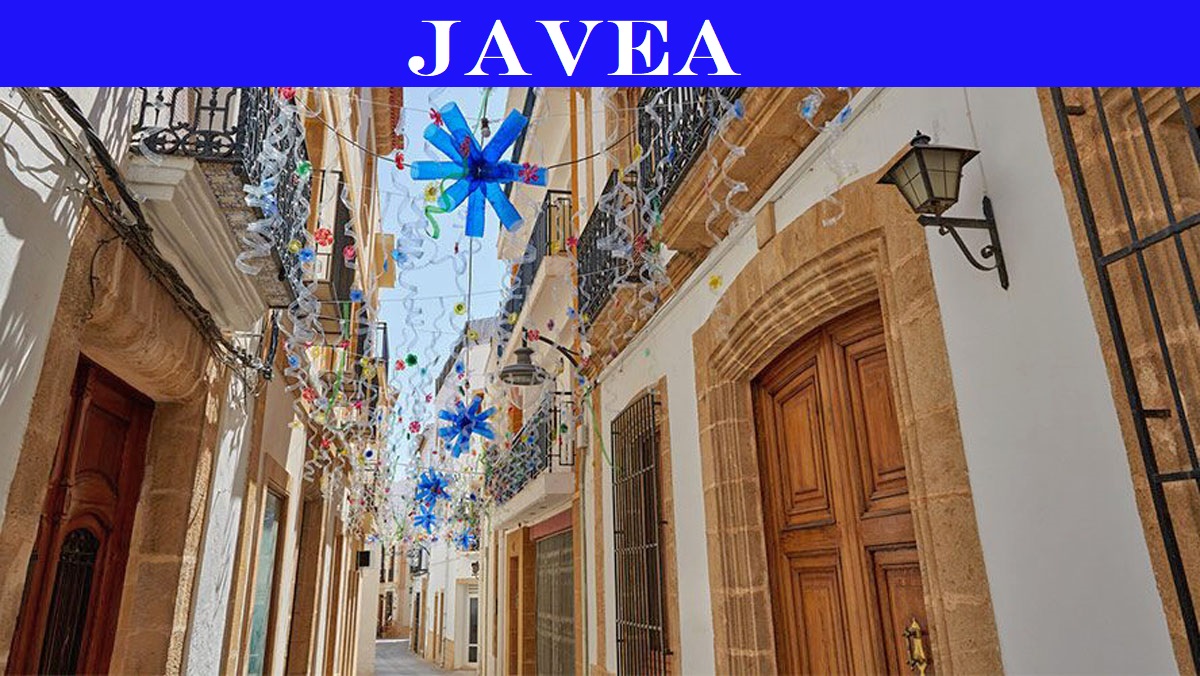 Enge Gasse im historischen Zentrum von Javea, mit traditionellen Steintüren, schmiedeeisernen Balkonen und festlichen Hängedekorationen mit blauen Sternformen.
