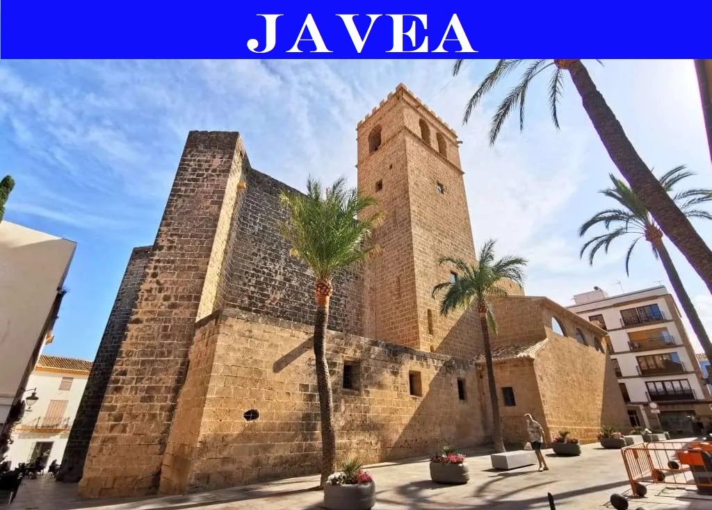 Historische Steinkirche mit Glockenturm in Jávea, mit robustem Mauerwerk und Strebepfeilern, auf einem sonnigen Platz mit Palmen.