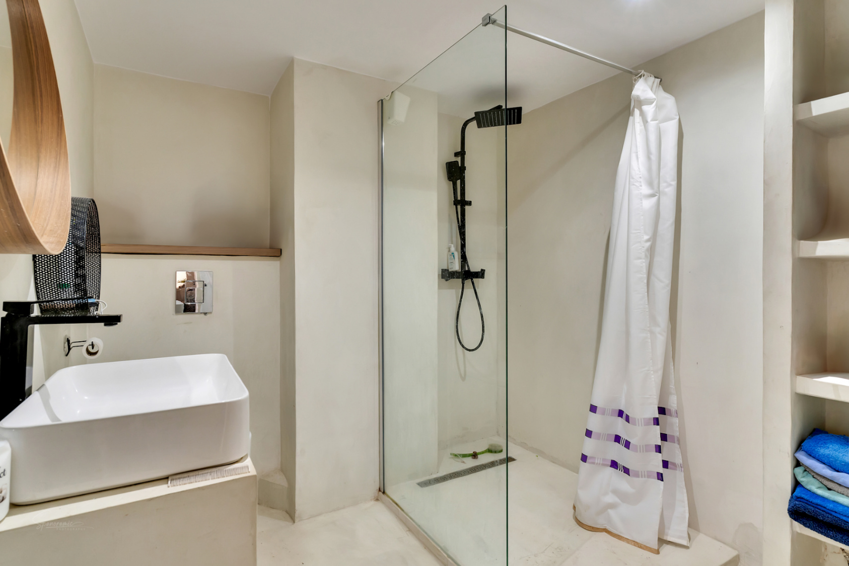 Modernes Badezimmer mit Aufsatzwaschbecken, mattschwarzen Armaturen und ebenerdiger Dusche mit Glaswand. Einzigartiger Holzspiegel und integrierte Regale.