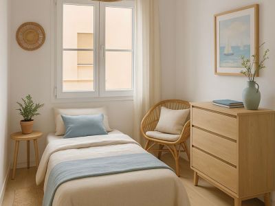 Einzelzimmer mit Bett in neutralen und blauen Tönen. Helle Holz- und Rattanmöbel, eine geflochtene Pendelleuchte und viel natürliches Licht vom Fenster.